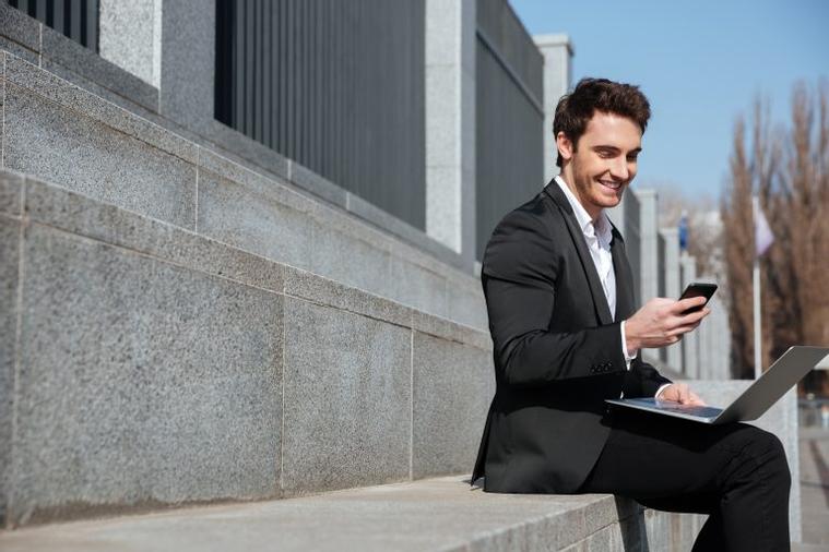 smiling-young-businessman-sitting-outdoors-chatting-by-phone-768x512