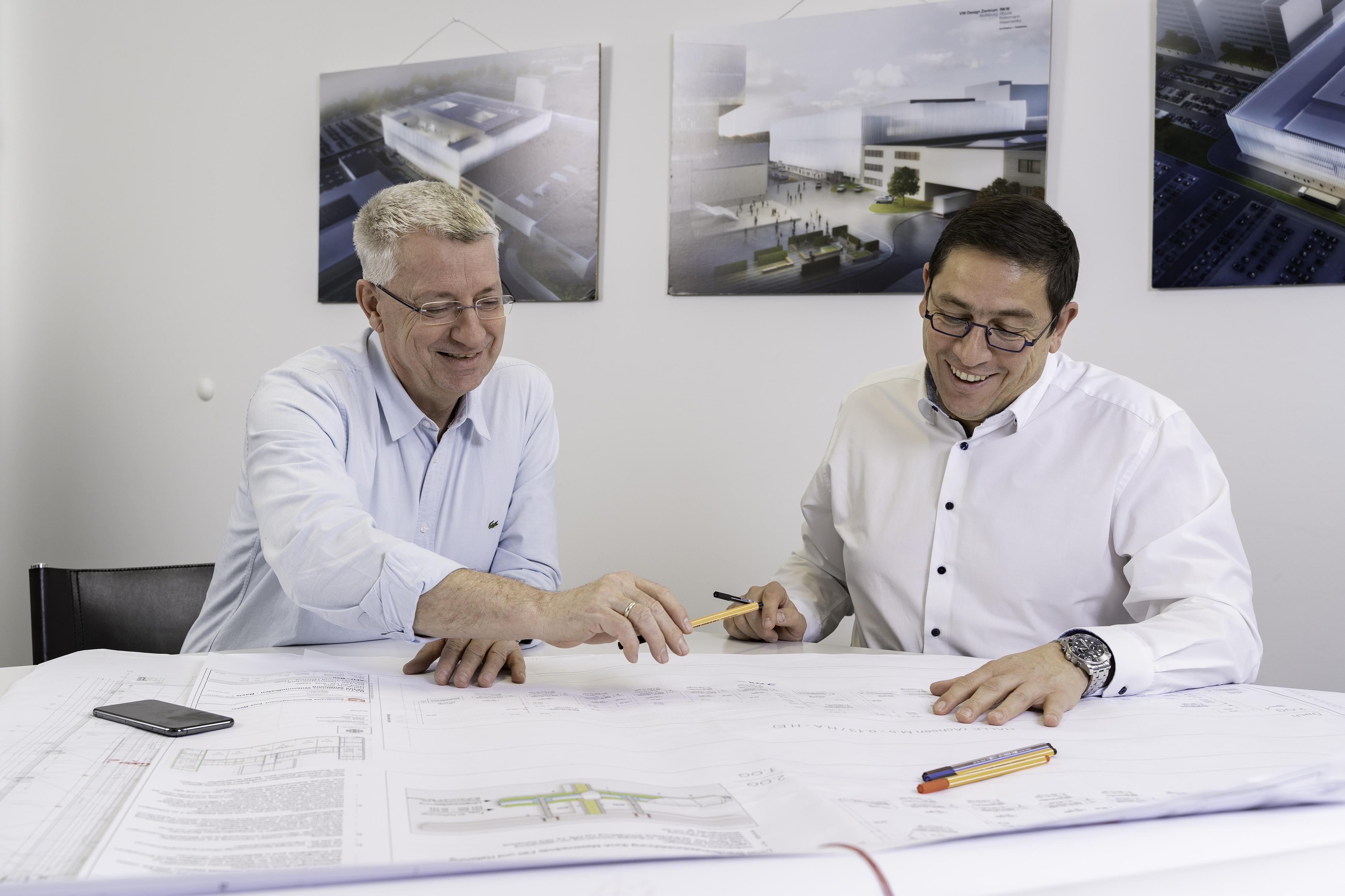 Meetingraum mit zwei Kollegen die über einen Architektenplan reden.
